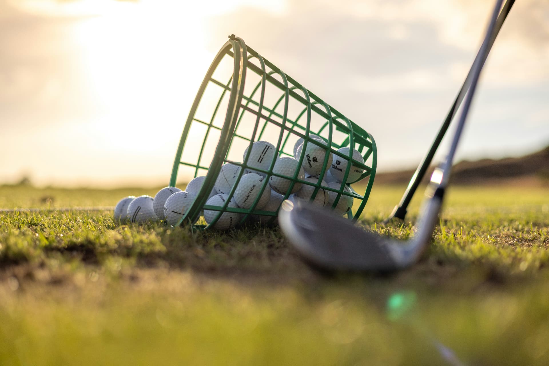 Bucket of balls and an iron on a driving range in morning light